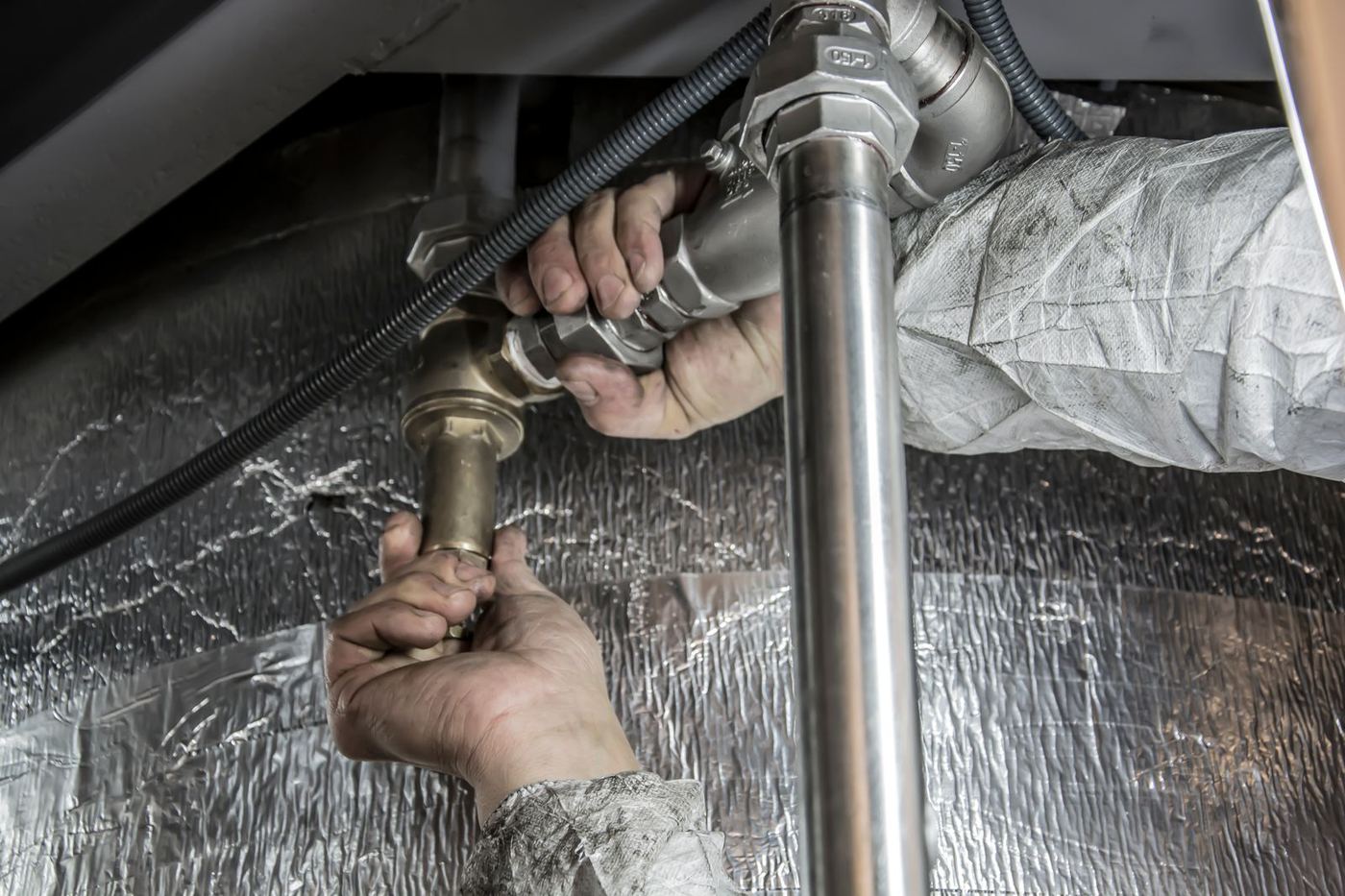 Plumber repairing a burst copper water pipe under a sink
